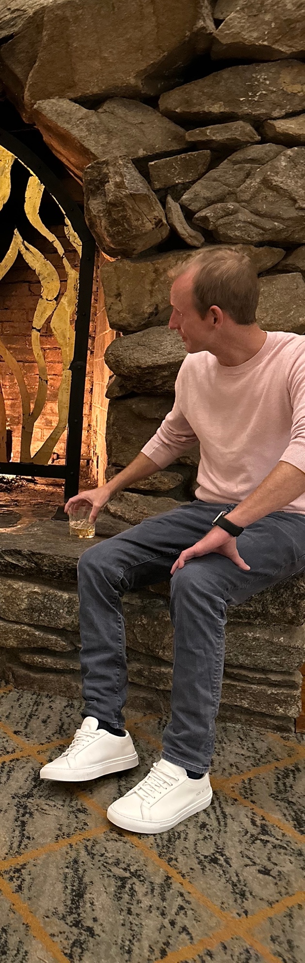 A person sitting on a stone ledge holding a drink

Description automatically generated